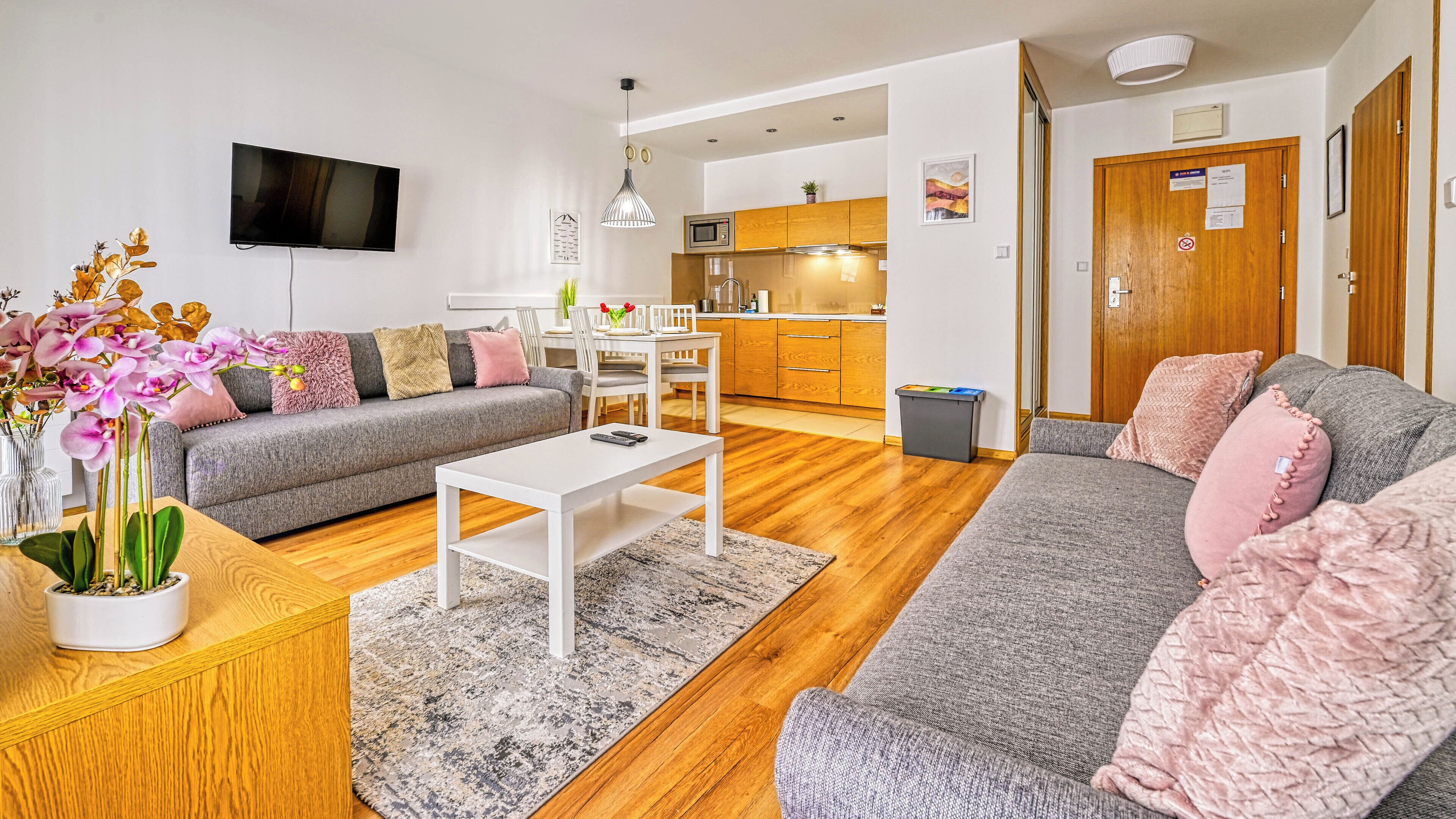 A modern living room with a grey sofa, a white coffee table, and a TV mounted on the wall.