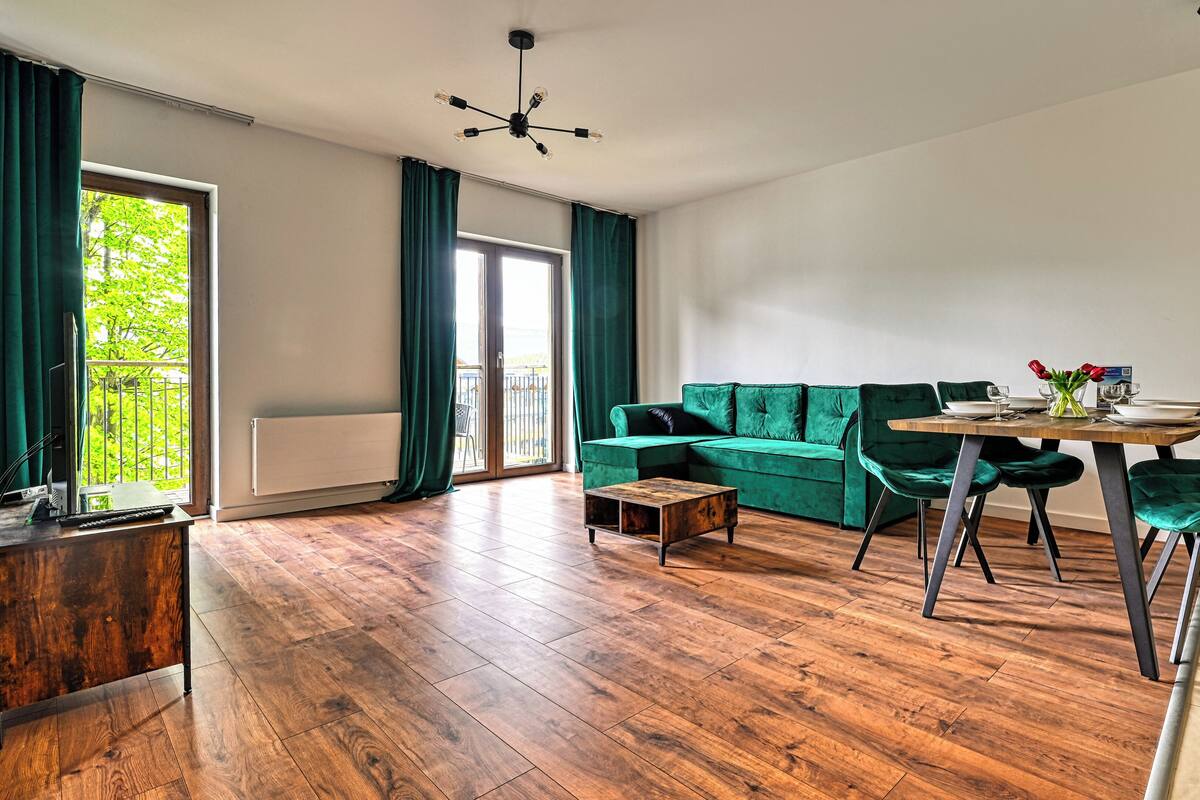 Una sala de estar moderna con un sofá modular, una mesa de comedor con sillas, una mesa de centro de madera y vistas a través de un ventanal.