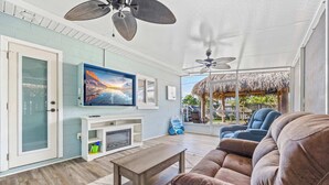 Una sala de estar con televisión, ventiladores de techo, un sofá y chimenea.