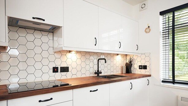 Et moderne køkken med hvide skabe, en træbordplade, en sort hane og bagvæg i hexagonfliser.