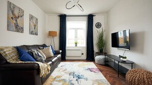 En stue med en lædersofa, et fjernsyn, en plante og kunst på væggen.