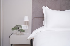 A neatly made bed with white bedding, a bedside lamp, and a small potted plant on a bedside table.
