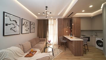 Un salon moderne avec un canapé, une table basse et des œuvres d’art. On aperçoit également un coin cuisine avec une table à manger et des tabourets de bar.