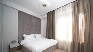 A modern bedroom with a large bed, a nightstand, a wall-mounted headboard, and sheer curtains. - Designer Apartment Steps Away from Main Attractions (Yerevan)