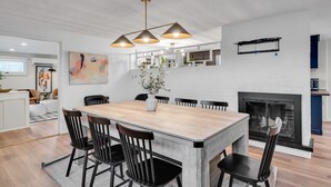 A modern dining area with a wooden table and black chairs, a white brick fireplace, and pendant lighting. - Luxury Boston Ranch –Sleeps 8|Pet+|Heated pool (Framingham)
