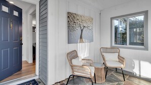 A room with a blue door, a white wall, and a large window. There are two wicker chairs and a small table. - Luxury Boston Ranch –Sleeps 8|Pet+|Heated pool (Framingham)