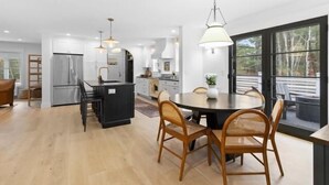 Een moderne keuken met een centraal eiland, een eetgedeelte met stoelen en grote ramen.