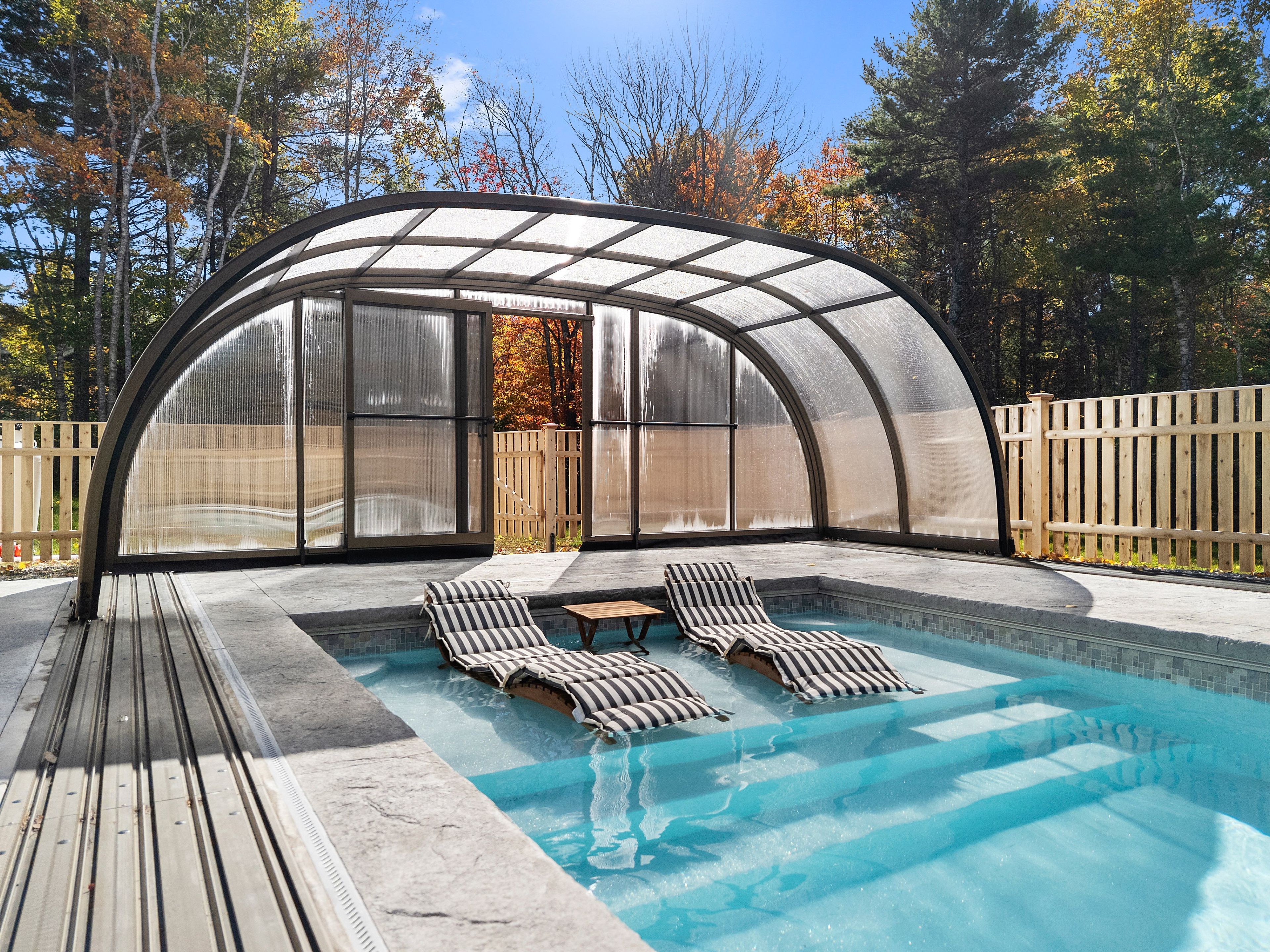 A covered outdoor swimming pool with lounge chairs and a glass enclosure.