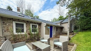 Une maison en pierre avec une terrasse en bois, du mobilier d’extérieur et une porte bleue.