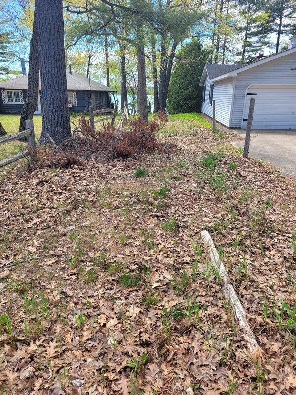 A residential area with a wooden fence, leaf-covered ground, and a house with a garage. - Catalina - Very Cute, Comfy, and Traditional!  Includes Window A/C Unit and 2 Kayaks! (Oscoda)