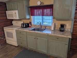 A kitchen with a stove, microwave, toaster, sink, and coffee maker. - Catalina - Very Cute, Comfy, and Traditional! Includes Window A/C Unit and 2 Kayaks! Dog-friendly as well! (Oscoda)