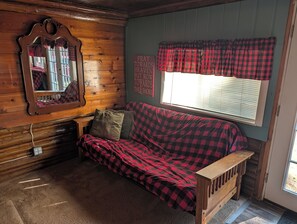 A cabin interior with a wooden bench, a red and black checkered sofa, a mirror, and a window with blinds. - Catalina - Very Cute, Comfy, and Traditional!  Includes Window A/C Unit and 2 Kayaks!  Dog-friendly as well! (Oscoda)