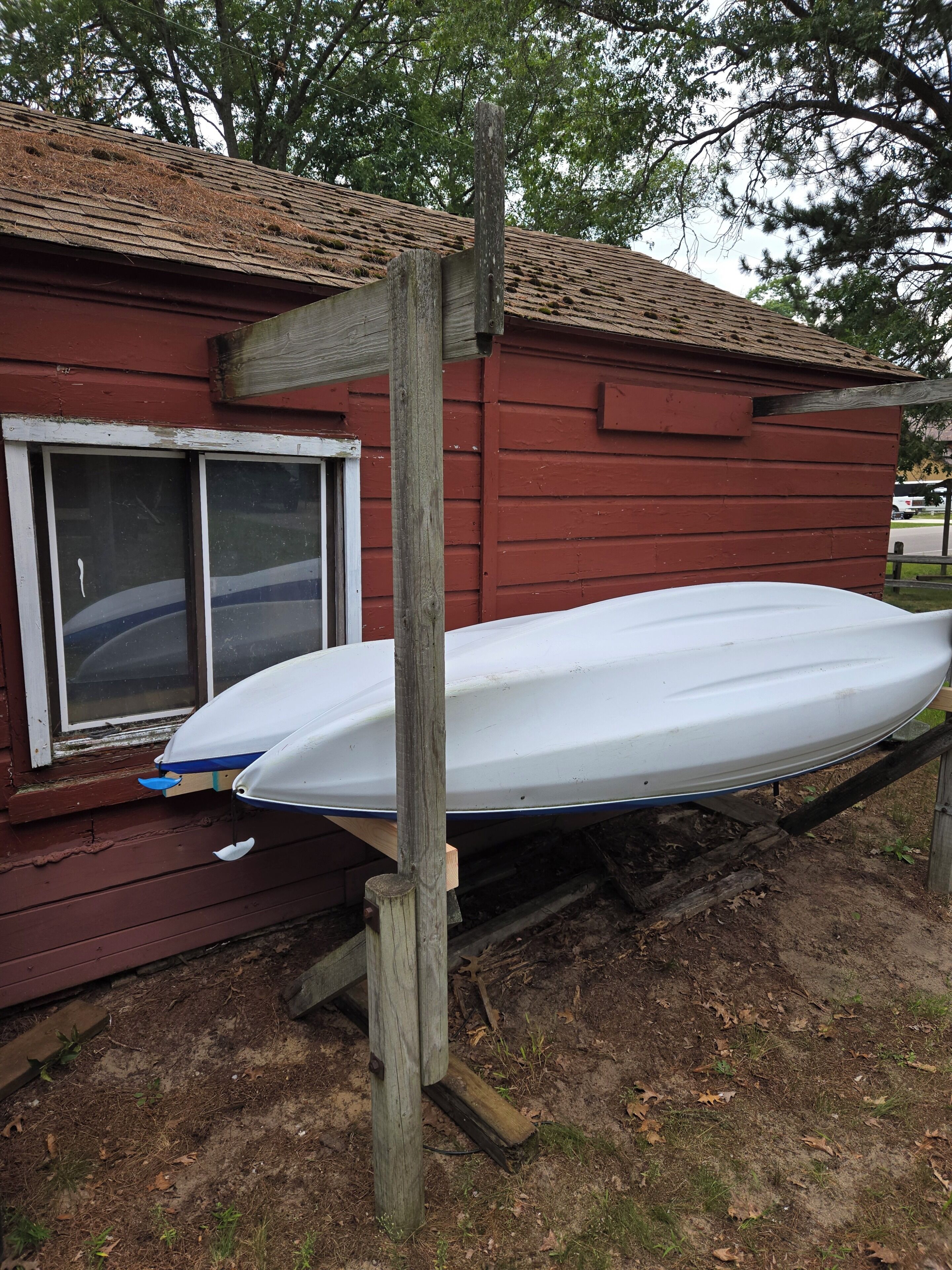 A white boat propped up against a red wooden building with a window.