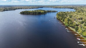 An aerial view of a lake with a docked boat area and a small island. - Catalina - Very Cute, Comfy, and Traditional!  Includes Window A/C Unit and 2 Kayaks! (Oscoda)