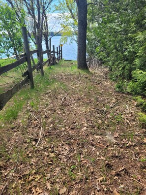 A natural landscape with a wooden fence, trees, and a body of water in the background. - Catalina - Very Cute, Comfy, and Traditional!  Includes Window A/C Unit and 2 Kayaks! (Oscoda)