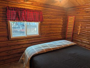A cabin room with a bed, a window with a view, and a red curtain. - Catalina - Very Cute, Comfy, and Traditional!  Includes Window A/C Unit and 2 Kayaks!  Dog-friendly as well! (Oscoda)