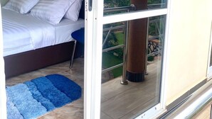 Une chambre à coucher avec un lit, un tapis bleu et une grande fenêtre donnant sur des arbres, ainsi qu’un balcon.