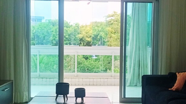 Een moderne woonkamer met een grote schuifpui naar een balkon, een donkere bank en een salontafel met twee zwarte potten.