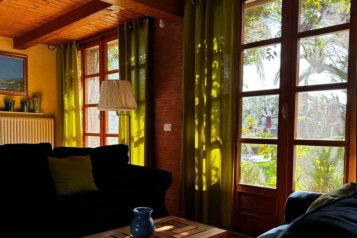 A cozy living room with a wooden ceiling, a sofa, a coffee table, and a window with green curtains.