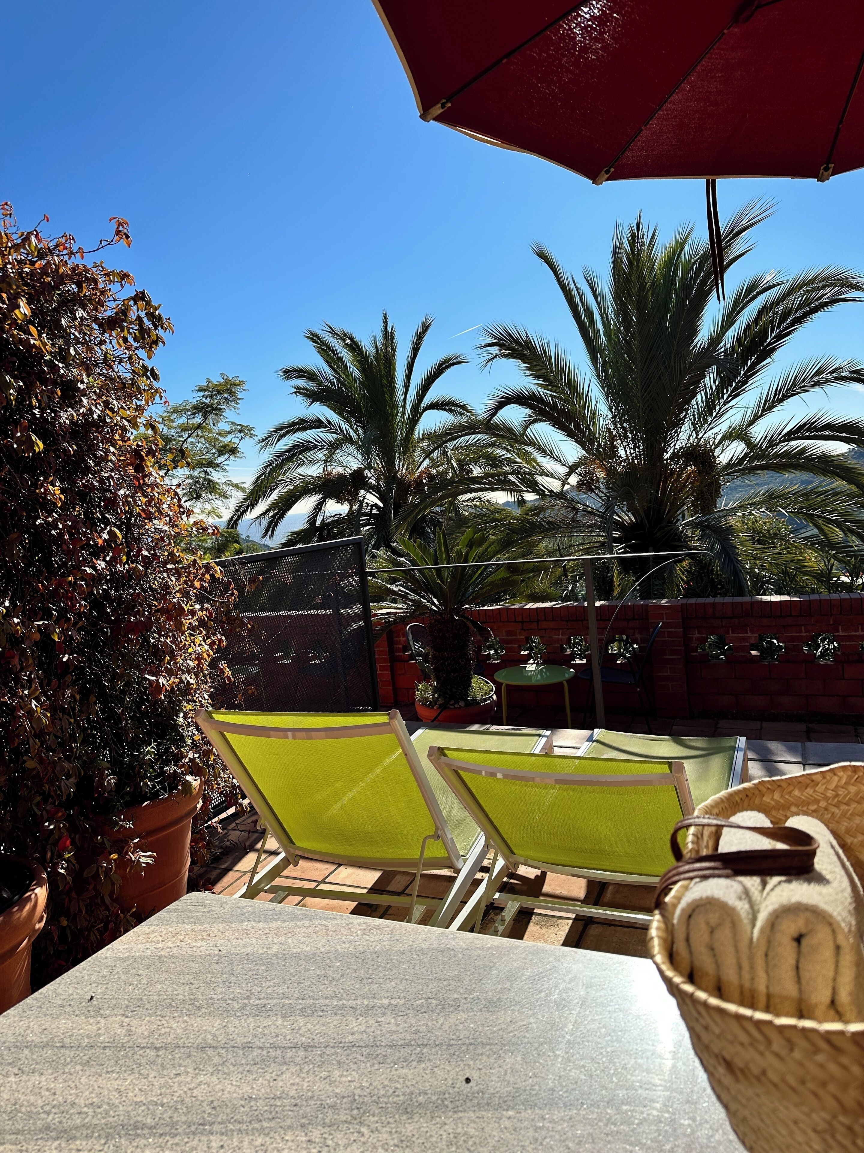 An outdoor patio area with a table and chairs, a red umbrella, and potted plants.