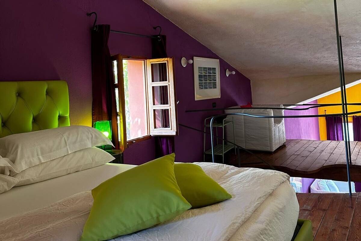 A bedroom with a bed, a window, and a view of another room.