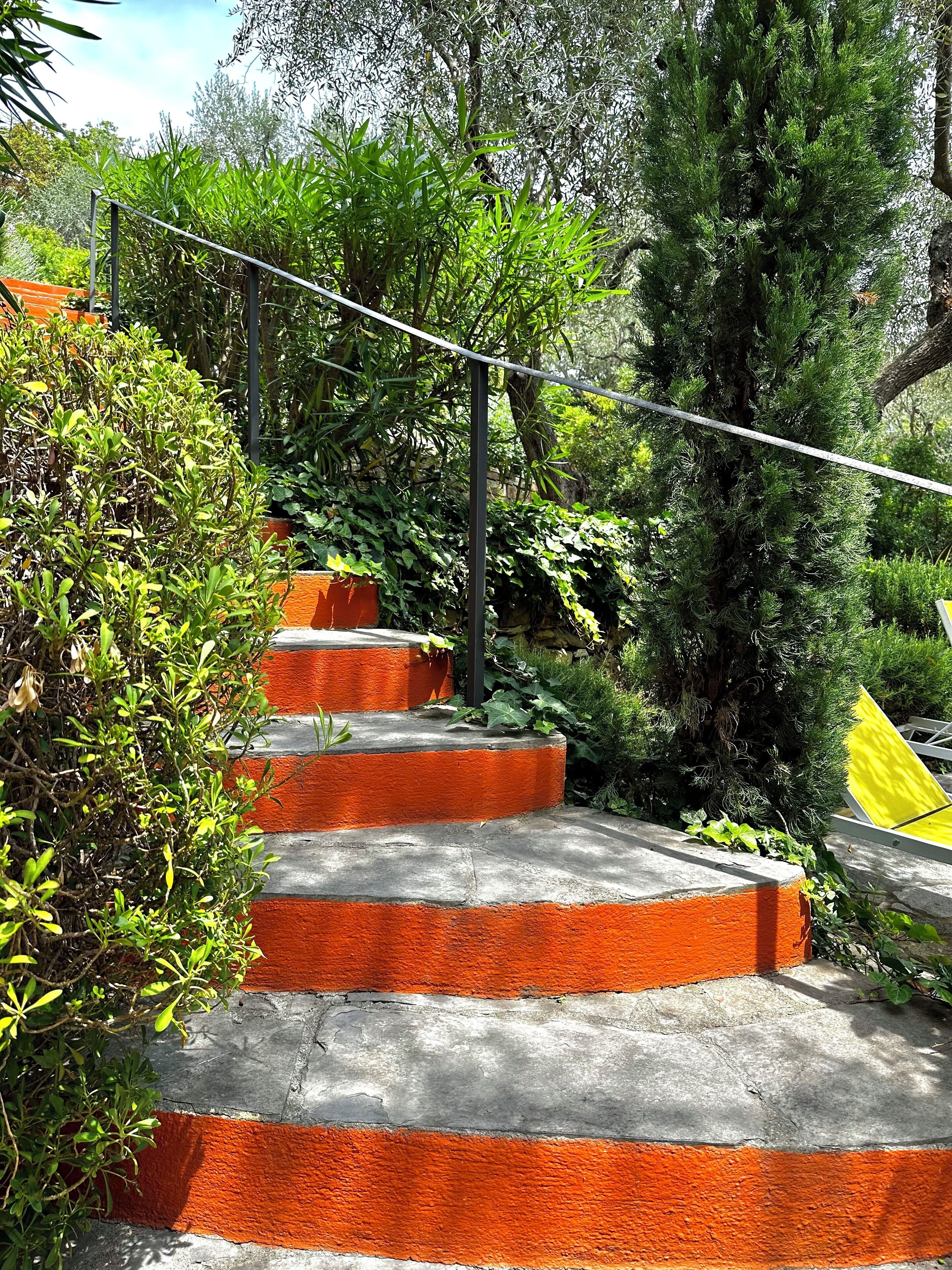 Un conjunto de escalones exteriores de hormigón con detalles en naranja, rodeado de vegetación exuberante y árboles.