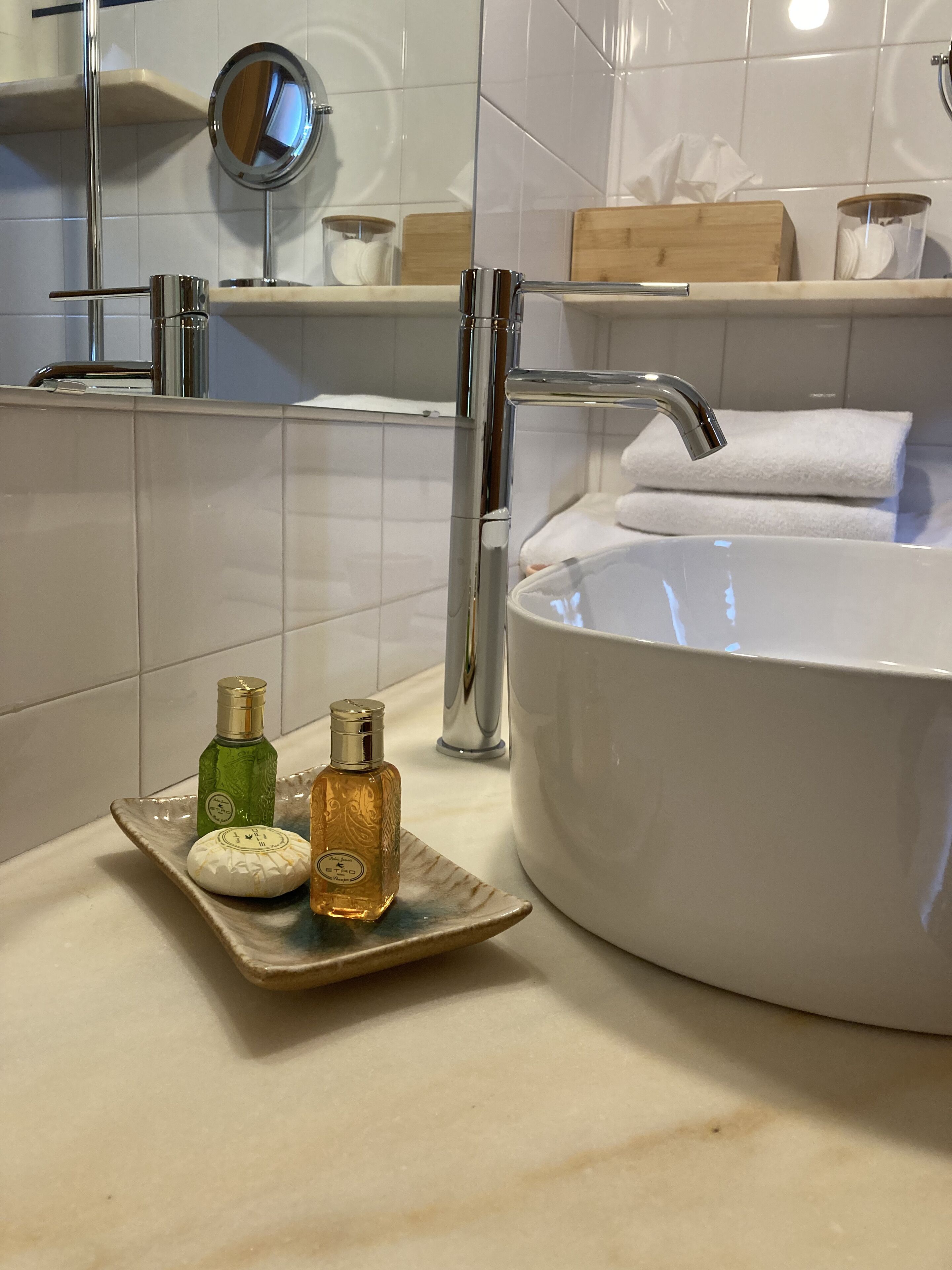 Une salle de bain avec un grand lavabo blanc, des robinets chromés et un petit plateau contenant deux bouteilles de liquide.