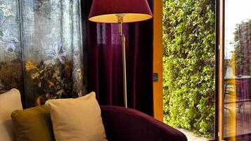 A room with a dark red sofa, a floor lamp, and a view of greenery through a glass door.