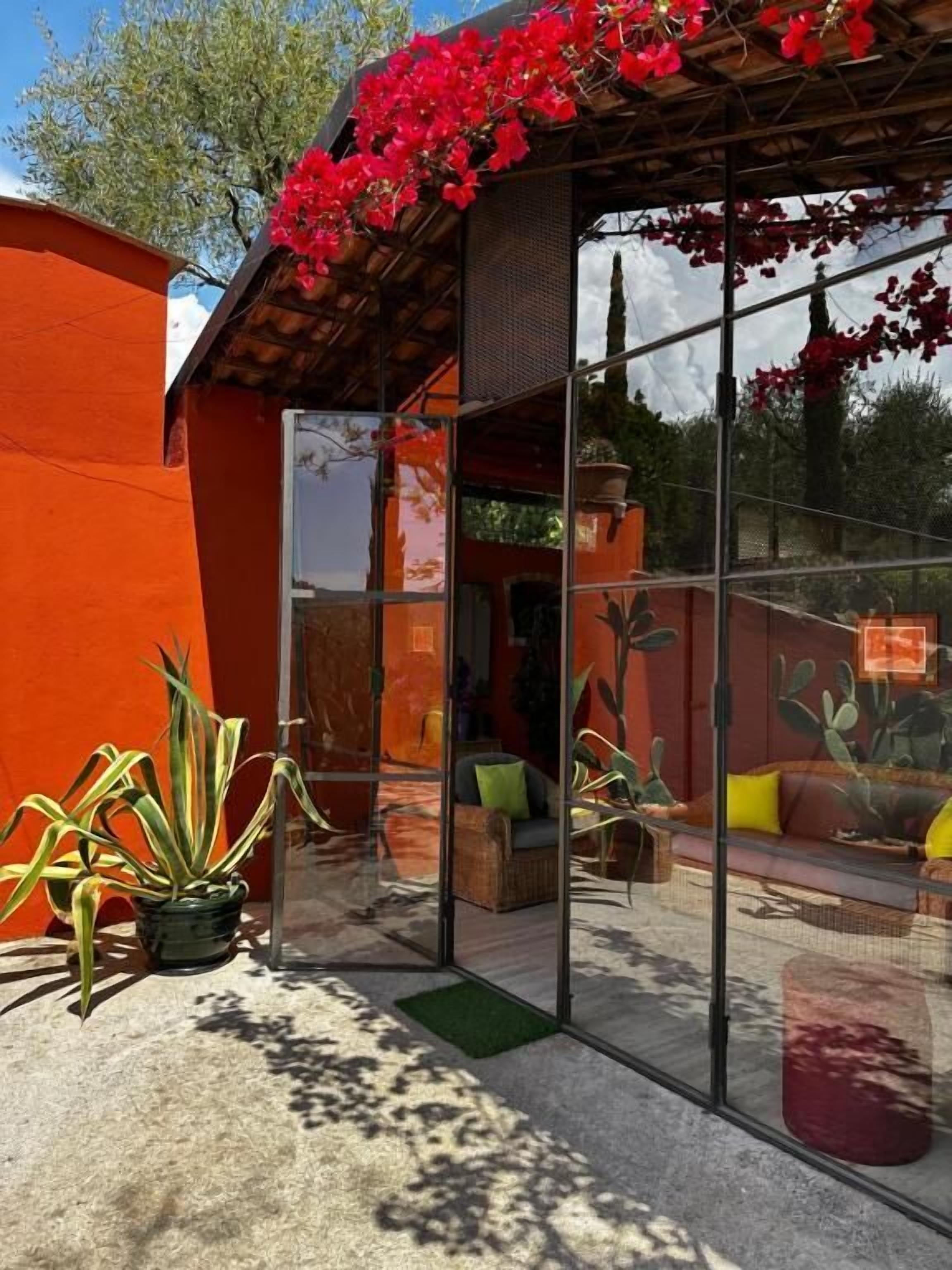 A modern house with a glass facade, a red exterior, and a patio area with plants and furniture.