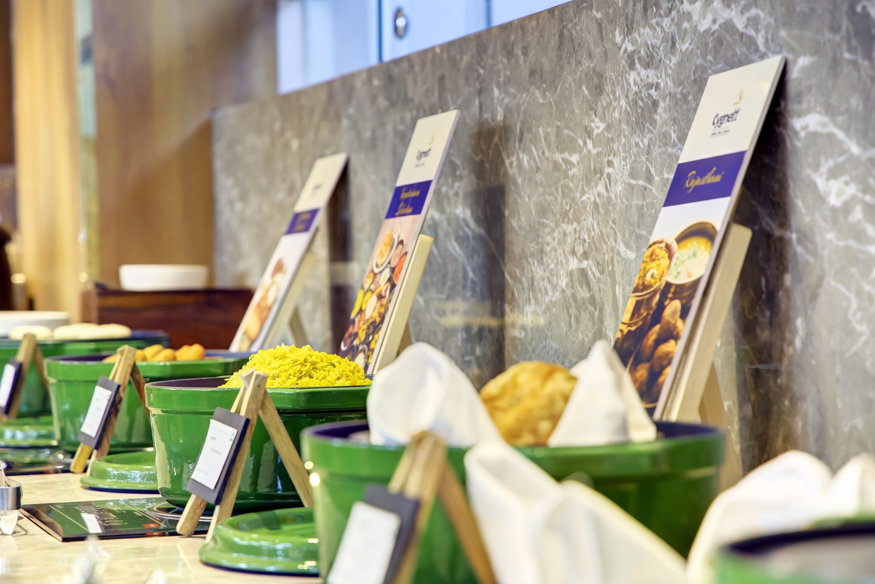 A buffet with labeled food containers and a marble countertop.