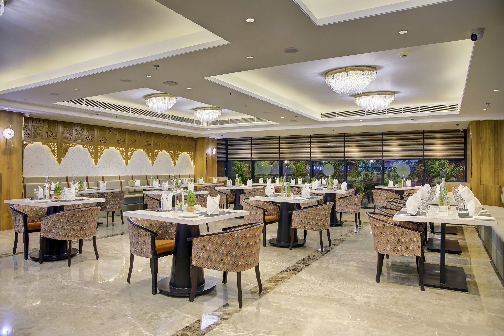Un vaste espace dédié à la salle à manger, avec de nombreuses tables et chaises, de magnifiques lustres et une vue sur une végétation tropicale.