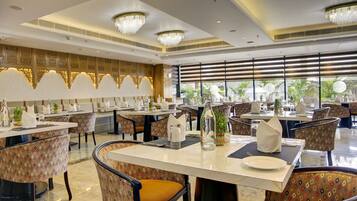 A spacious dining area with multiple tables and chairs, chandeliers, and large windows with views of greenery.