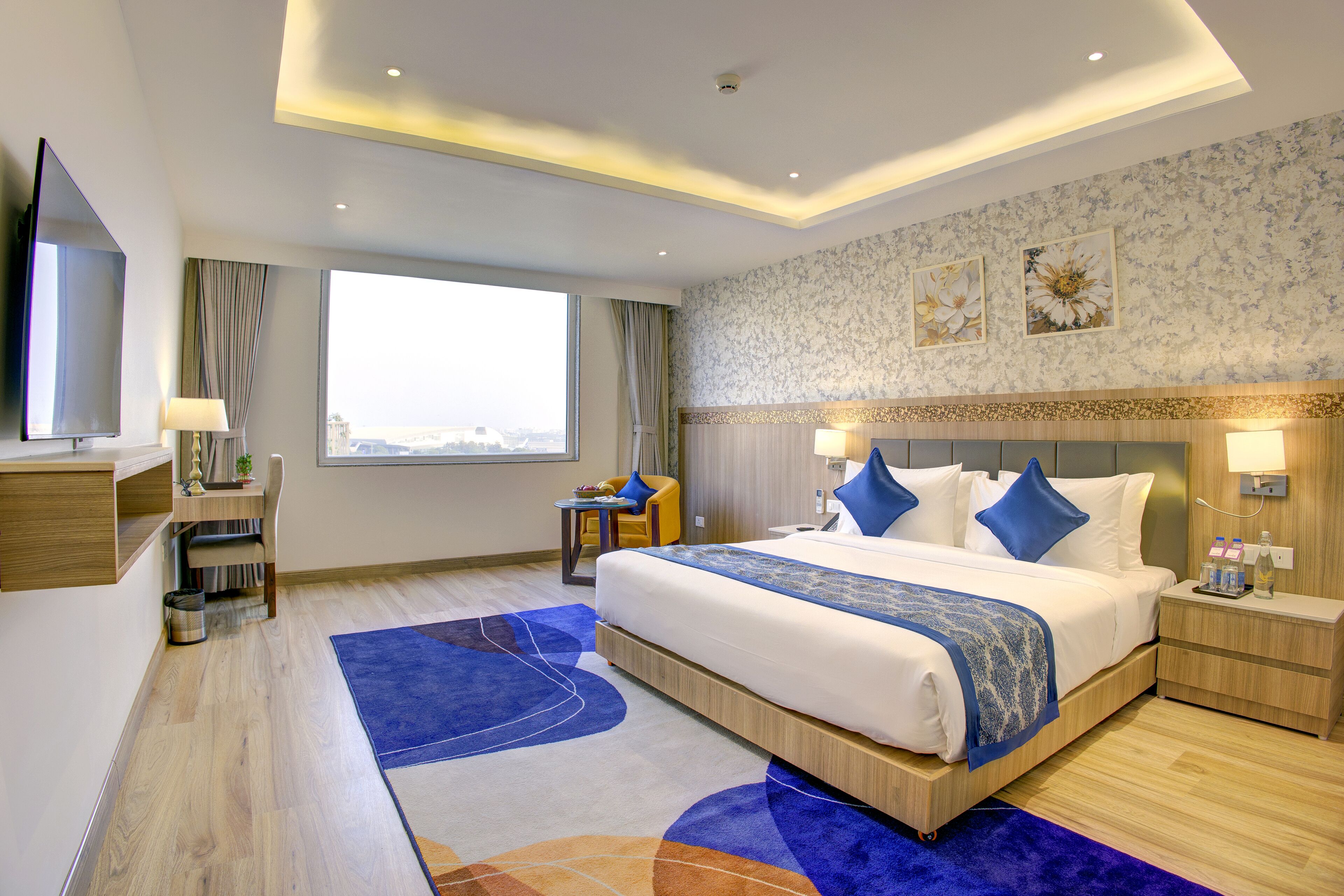 Ein modernes Hotelzimmer mit einem großen Bett, einem Schreibtisch, einem Sessel, einem Fernseher und Blick auf die Stadt.