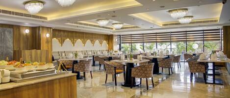 Un comedor amplio con varias mesas redondas y sillas, candelabros y un mostrador de buffet con diversas opciones de comida.