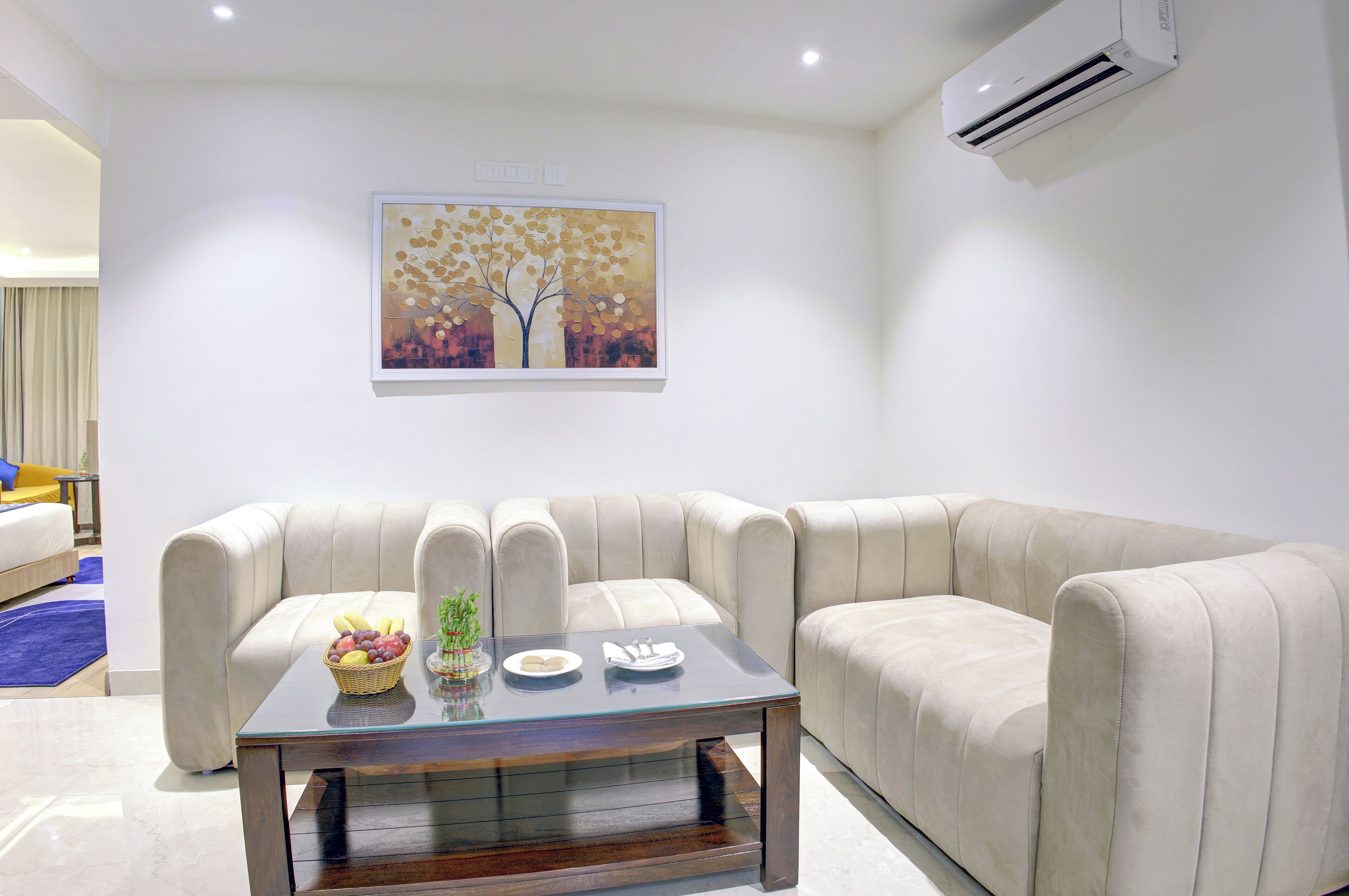 A modern living room with a beige sectional sofa, a glass coffee table, and a wall-mounted air conditioner.