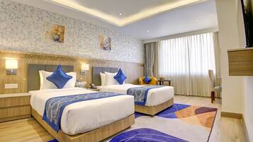 A hotel room with two beds, a desk, a chair, and a large window with curtains.