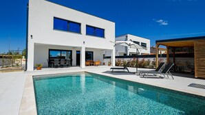 Ein modernes, zweistöckiges Gebäude mit Swimmingpool, Außenbereich zum Sitzen und überdachtem Bereich.