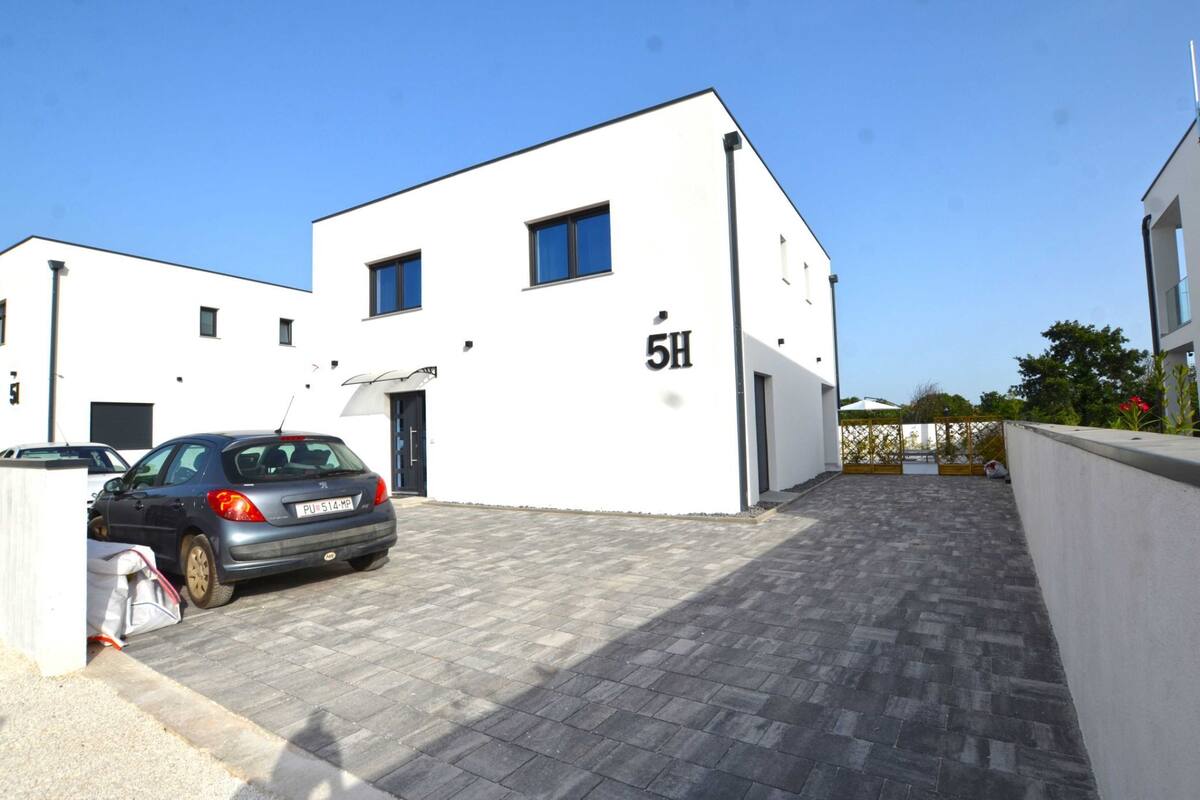 A modern building with the number 5H on its facade, a paved driveway, and a parked car.