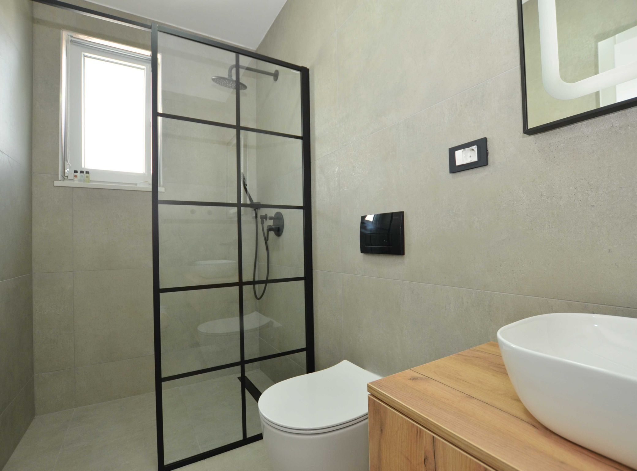 A modern bathroom with a glass-enclosed shower, a white toilet, and a wooden vanity with a large sink.
