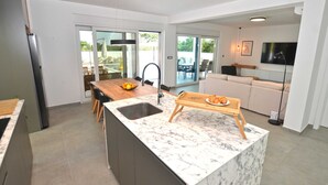 Eine moderne Küche mit einer Marmorarinsel, ein Essbereich mit Holztisch und ein Wohnbereich mit Sofa und Fernseher.
