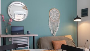Een moderne kamer met blauwgroene wanden, een ronde spiegel, een laptop, een droomvanger en een rond tafeltje met geweven onderzetters.