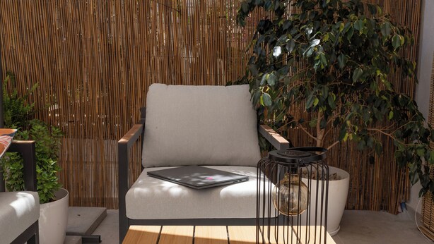 Een modern buitenverblijf met een houten tafel, twee stoelen, een comfortabele bank en een bamboe hek op de achtergrond.