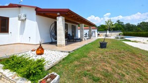 Una casa con un porche cubierto, mobiliario de exterior y una piscina.