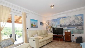 Una sala de estar con un sofá color beige, televisión y un mural en la pared.