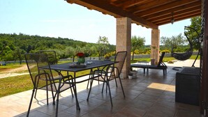 Un patio al aire libre con una mesa, sillas y una hamaca colgante, con vistas a un paisaje verde exuberante.