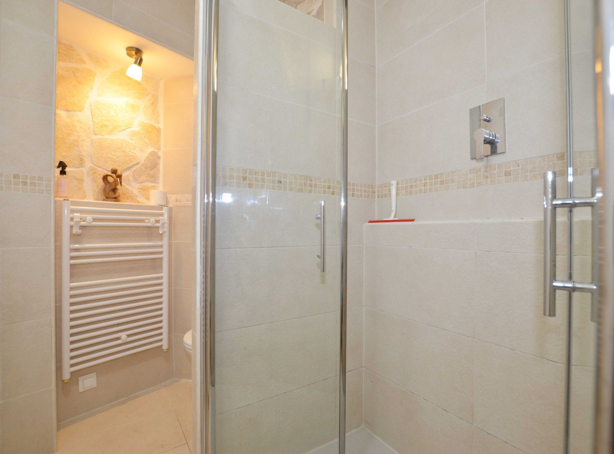 Un baño moderno con cabina de ducha de vidrio, un perchero blanco y un revestimiento de pared de piedra.