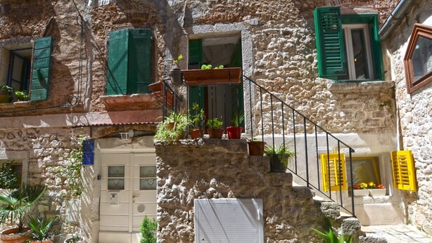 Un edificio in pietra con una scala, piante in vaso e una porta con insegna blu.