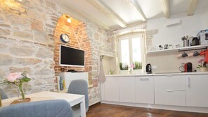 Una cucina accogliente con parete in pietra, pavimento in legno, mobili bianchi e televisore a schermo piatto.