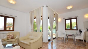 A spacious living area with a beige sofa, a glass table, and a dining table with chairs. There are large windows with curtains, a ceiling fan, and a microwave on a counter. - Elegant and Brigth Corner Apartments (Rovinj)