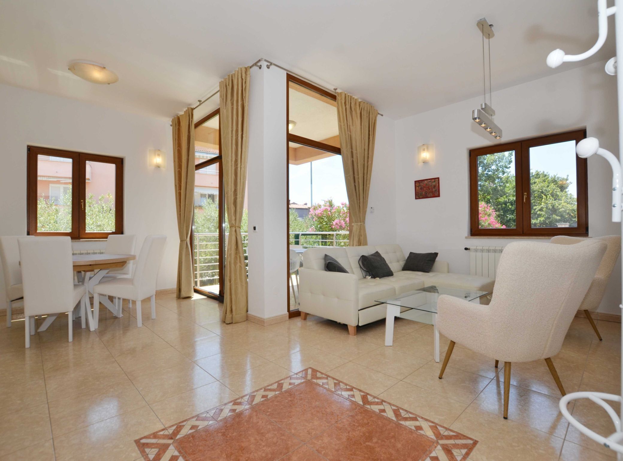 A spacious living room with a white sofa, a dining table with chairs, and a large sliding glass door leading to a balcony.